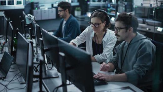 Young Team of Specialists Working on Desktop Computers and Having a Conversation at a Workplace. Female and Male Software Developers Discussing a Solution for Their Artificial Intelligence Project