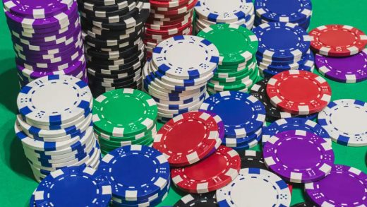 stacks of red white blue green black purple casino chips or betting chips on green gambling or gaming table