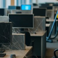 Bokeh photo of inside a modern, open it department in a modern, bright office that has no people. rows of cubicles are visible with computers that are turned off. the office is mostly clean and bright but cobwebs are visible on the workstations.. the