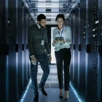 Male and Female Server Technicians Working in Data Center. Running Rack Server Diagnostics. Woman Uses Tablet Computer.