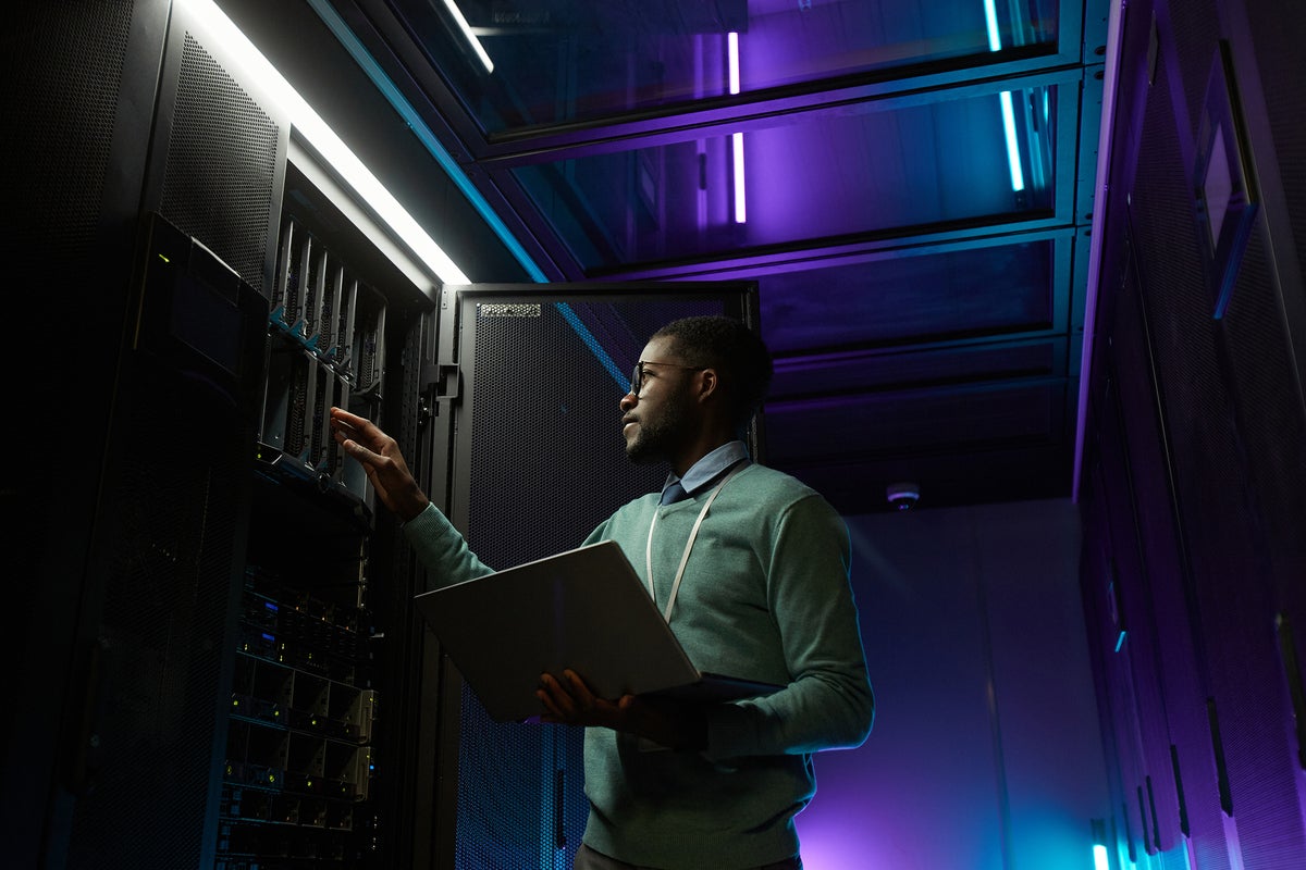 A developer / engineer / technician works with servers and a laptop in a data center.