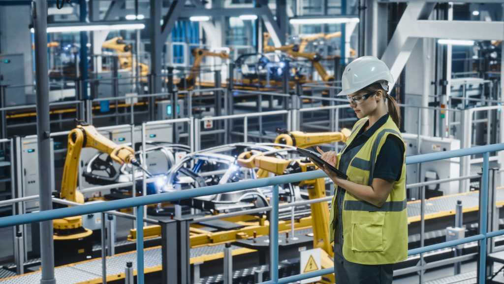 Female Car Factory Engineer in High Visibility Vest Using Tablet Computer. Automotive Industrial Manufacturing Facility Working on Vehicle Production with Robotic Technology. Automated Assembly Plant.