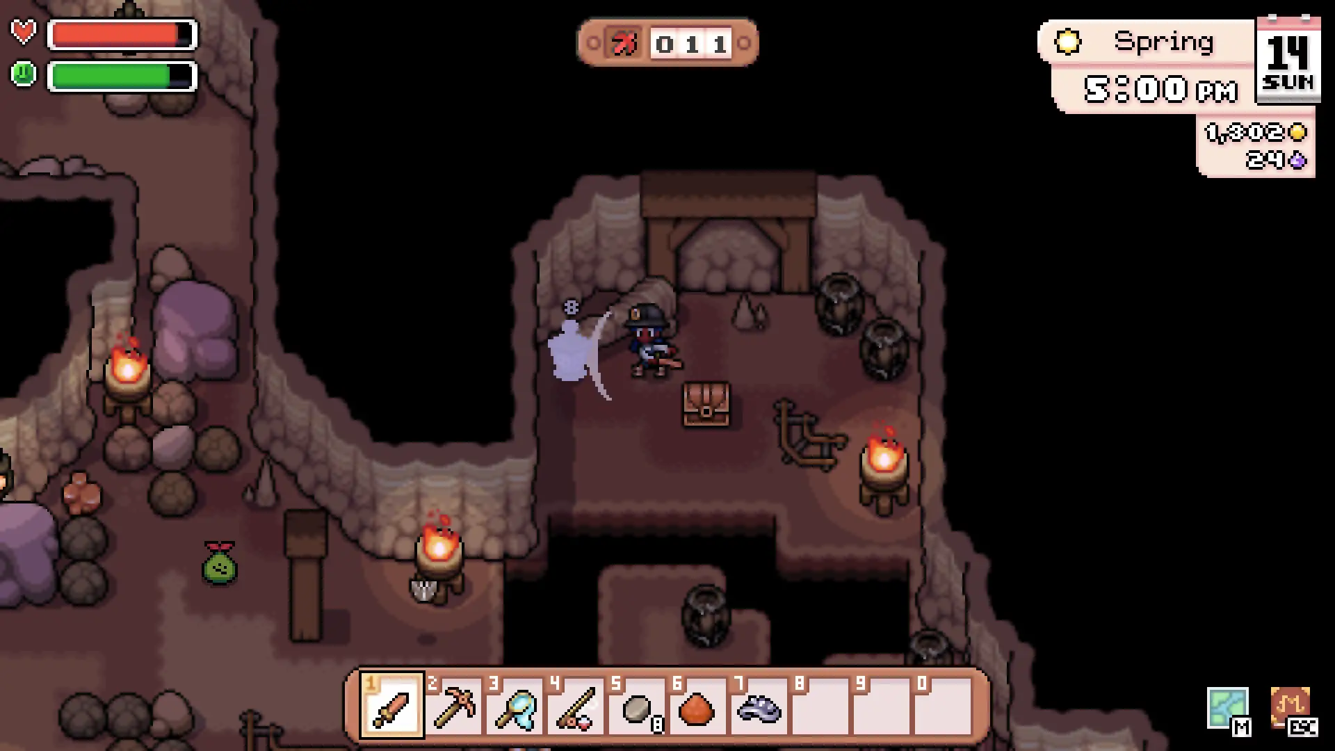 The farmer fights a floating enemy on a torchlit mine floor in Fields of Mistria, with ore, barrels, crates and a treasure chest in the cave