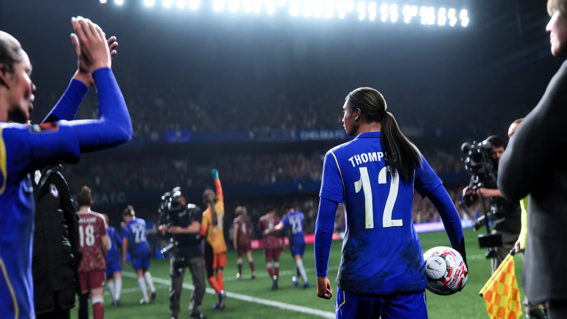 A player in a blue kit wearing number 12 walks to take a throw in while a teammate claps from the touchline