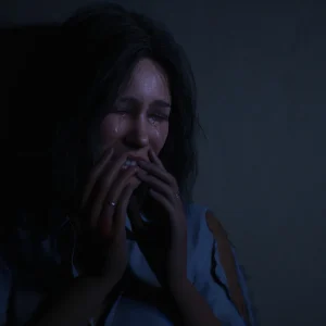 A young woman crying with both hands over her mouth while hiding in a dark corner