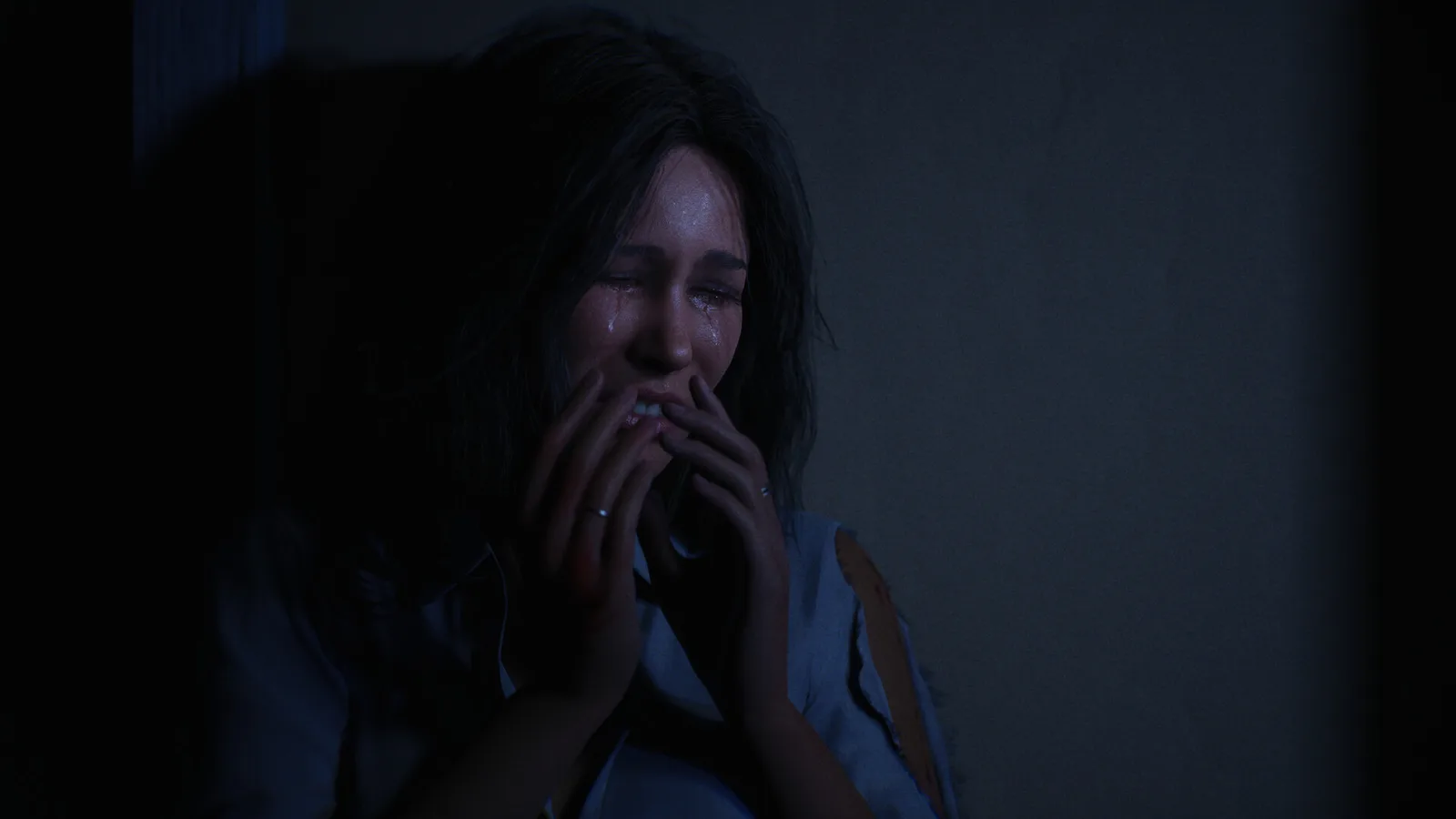 A young woman crying with both hands over her mouth while hiding in a dark corner