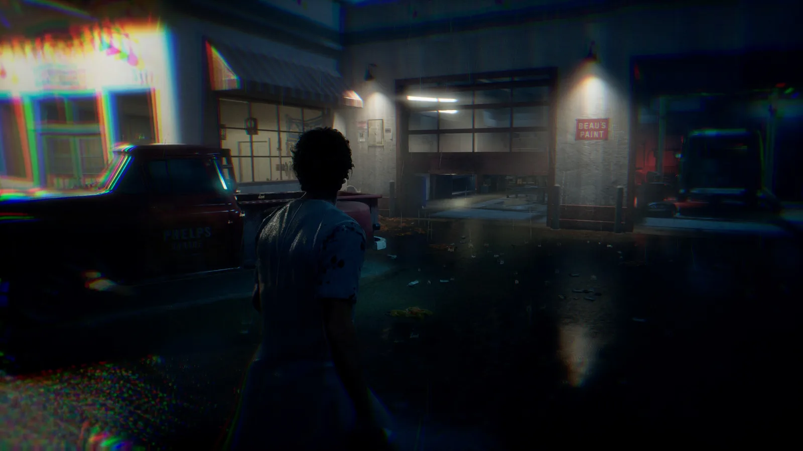 A civilian seen from behind on a wet Haddonfield street facing Phelps Garage and a paint store at night