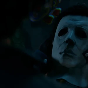 Close-up of Michael Myers in his white mask held by a gloved hand in dim blue light