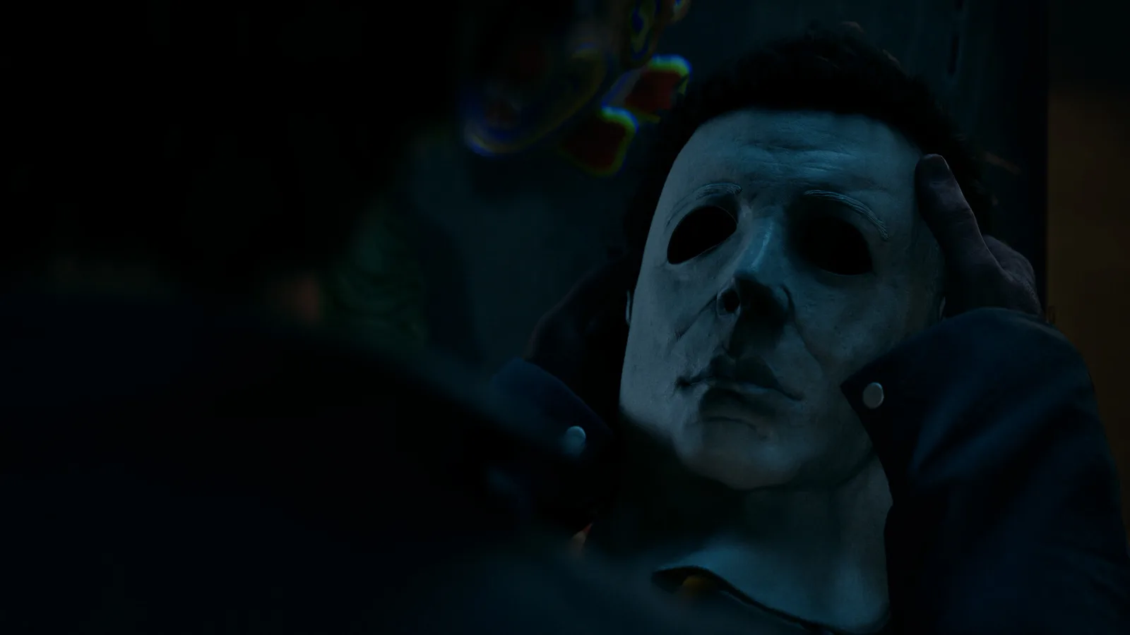 Close-up of Michael Myers in his white mask held by a gloved hand in dim blue light