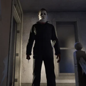Michael Myers standing on a pale upstairs landing holding a knife down at his side