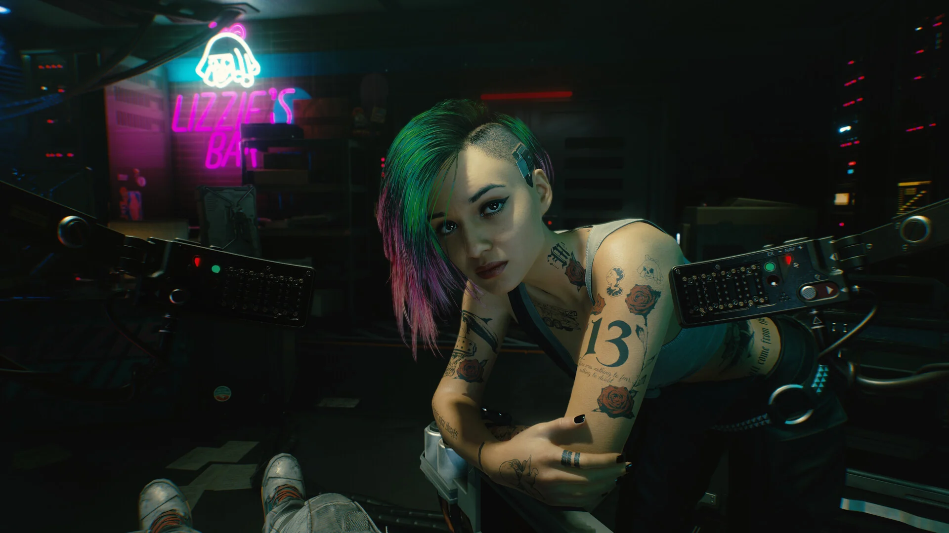 Judy Alvarez, with green and pink hair and tattooed arms, sits in a dim room lit by neon signs