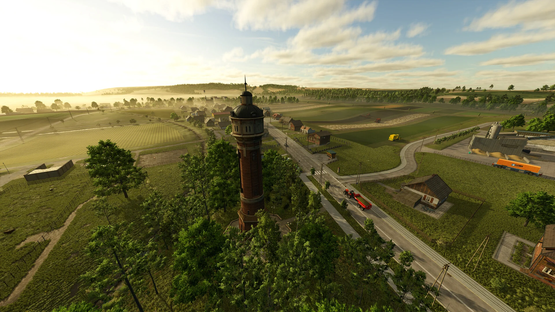 An aerial view of a Farming Simulator 25 valley with green fields, farm buildings, a road and a brick water tower in the foreground