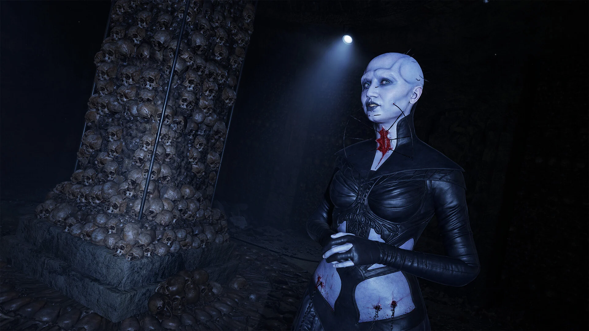 A pale female Cenobite in black leather stands under a spotlight beside a pillar built from stacked skulls