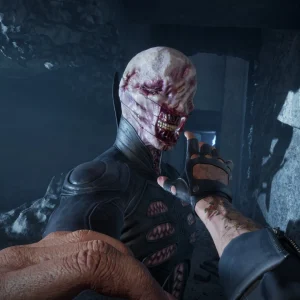 First-person view of the player grabbing a disfigured enemy with a torn, bloody face in a rocky cave passage
