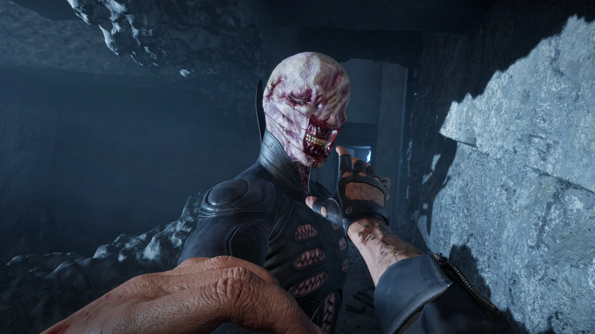 First-person view of the player grabbing a disfigured enemy with a torn, bloody face in a rocky cave passage