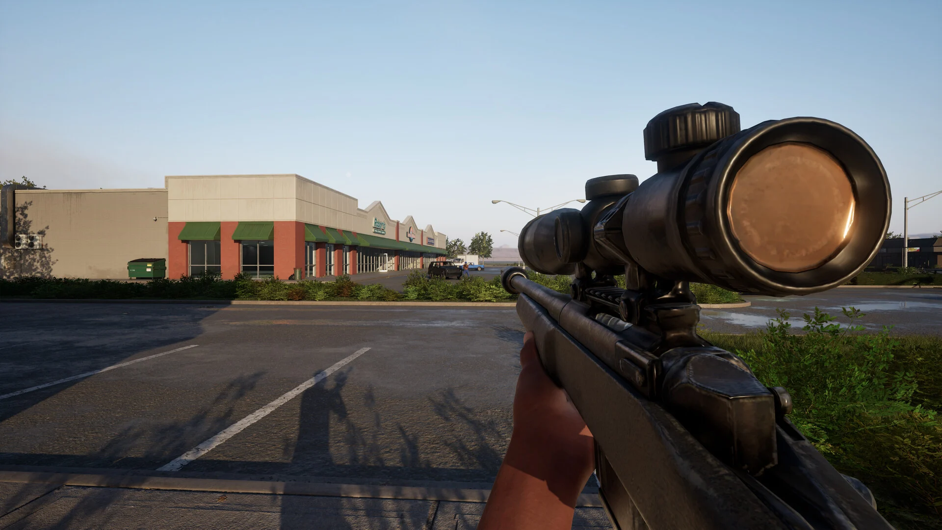 First-person view holding a scoped bolt-action sniper rifle in an empty parking lot outside a row of shops on a clear day