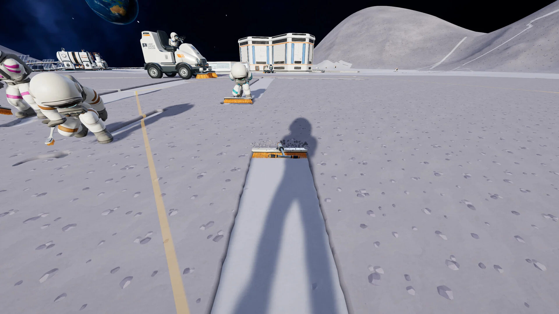 First-person view of a freshly cleaned strip of Moon ground, with another astronaut, a sweeper and a base building in the distance