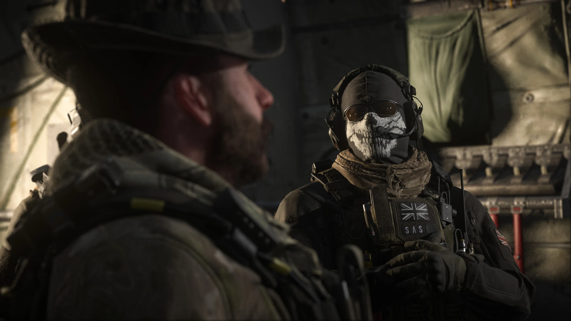 Captain Price in a boonie hat sits beside Ghost in his skull face mask inside a dim aircraft in Call of Duty: Modern Warfare III