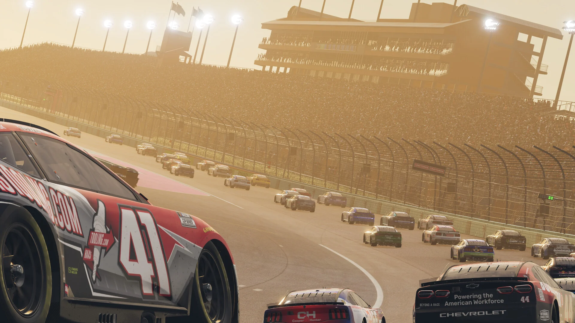 The No. 41 car leads a long pack of stock cars around an oval at sunset, with grandstands lit by low golden sunlight