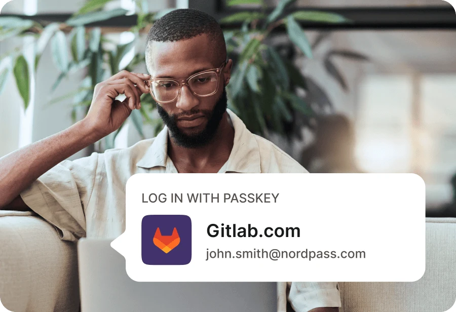 NordPass Log in with passkey prompt for a Gitlab.com account, next to a man looking at his laptop