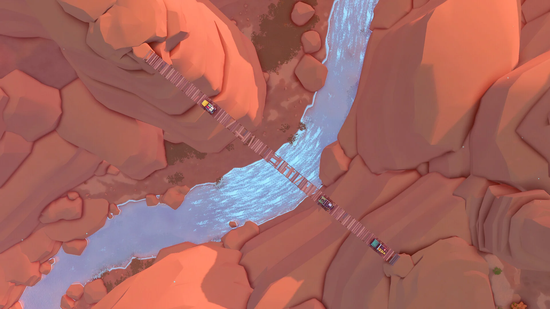 Top-down view of a small 4x4 crossing a long plank bridge over a river in a red rock canyon
