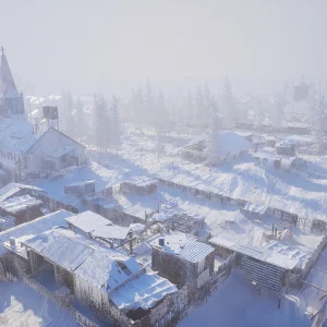 Aerial view of a snow-covered settlement with wooden houses and a church spire, surrounded by pine forest in thick fog