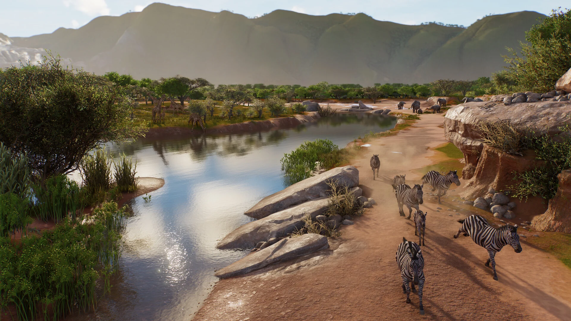 A herd of zebras walks along a sandy riverbank in a wide Planet Zoo 2 Wildlife Reserve, with mountains in the distance