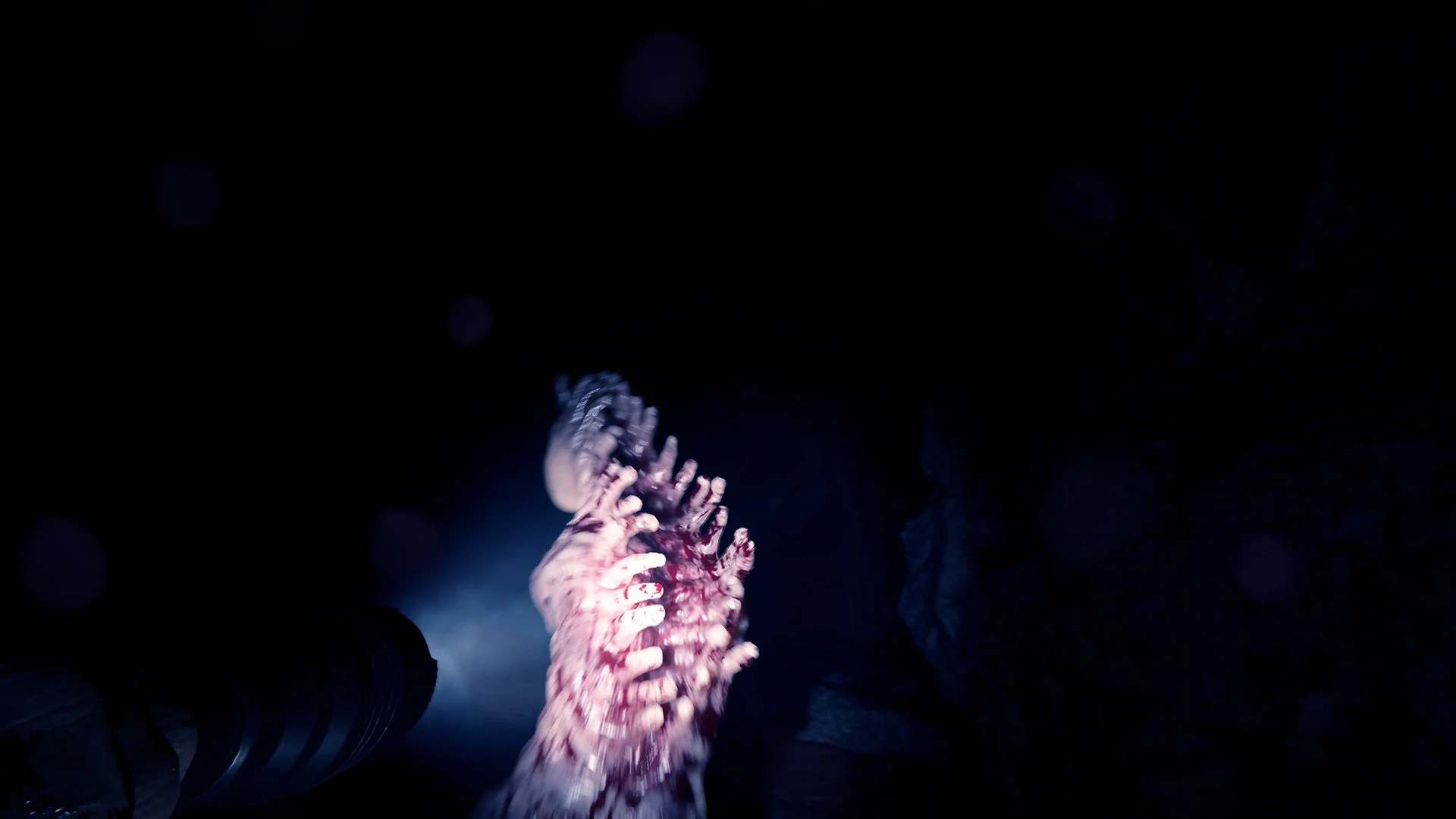 A pale, many-limbed mutant lit by a flashlight in a pitch-black cave