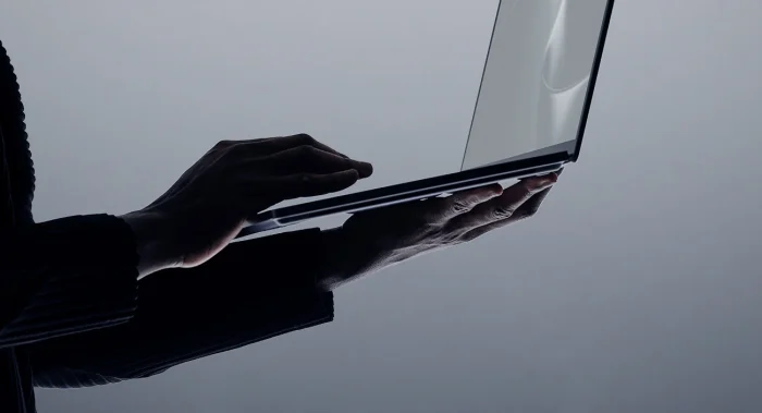 Person using the large haptic touchpad on Surface Laptop Ultra, shown in silhouette against a grey background