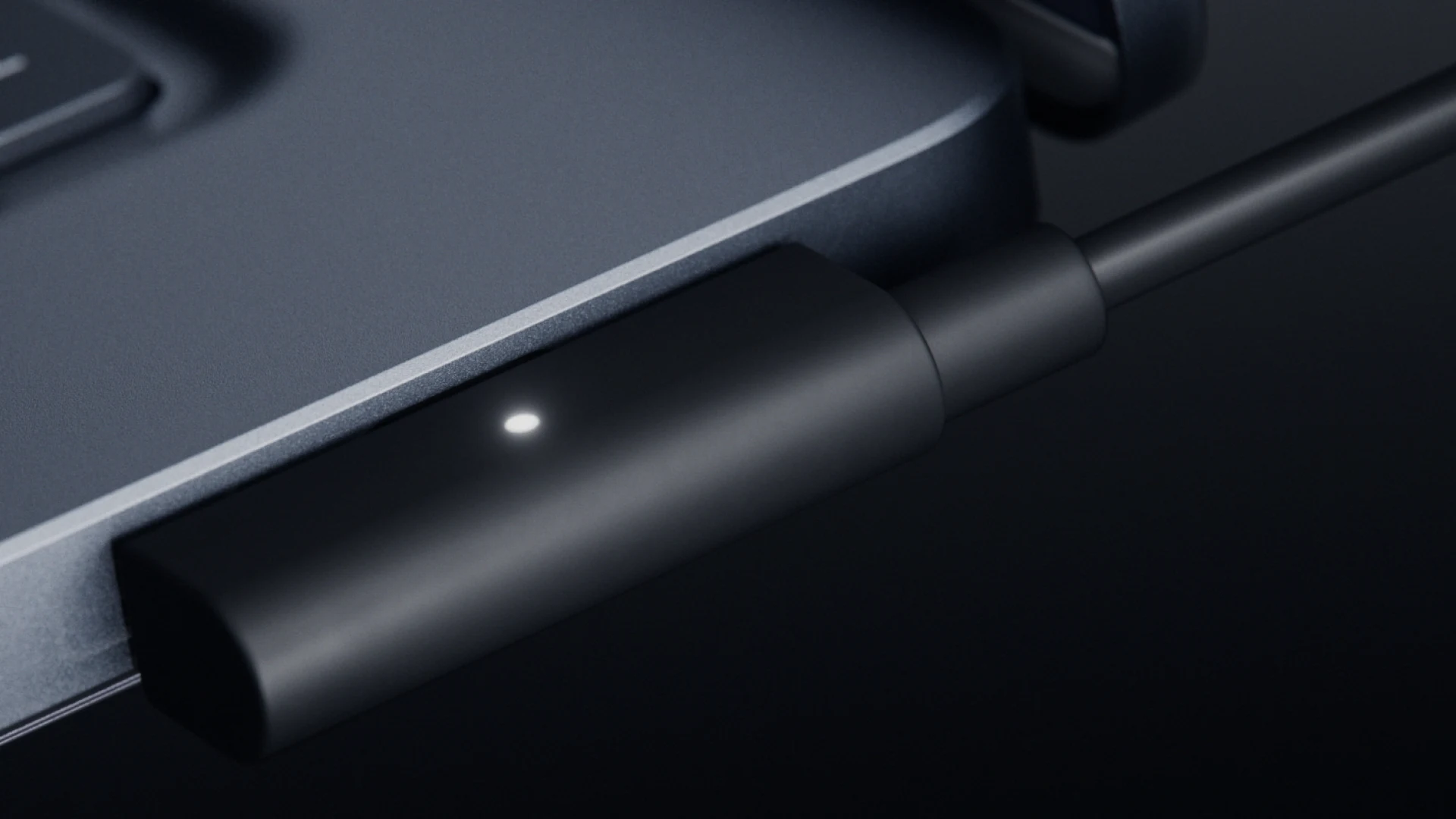 Black magnetic USB-C charging cable clipped to the side of a Surface Laptop Ultra with a small white status light