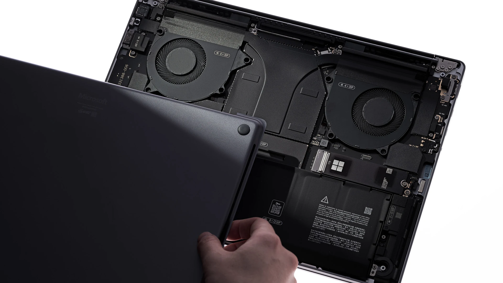 Hand lifting the bottom cover off Surface Laptop Ultra to show two cooling fans, the battery and the removable SSD