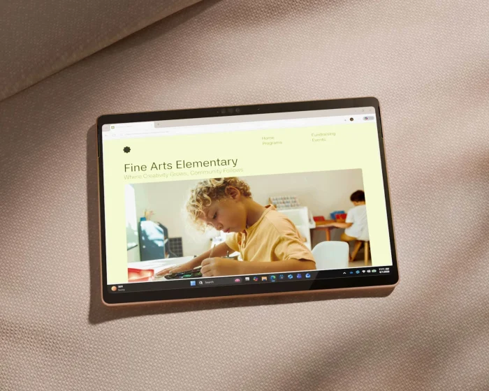 A Dune Surface Pro lying flat on a beige sofa in tablet mode with a school website on screen