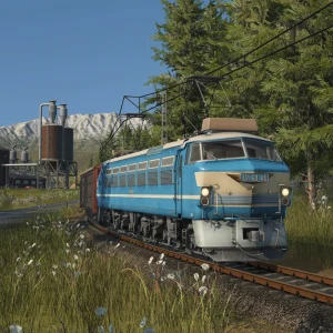 A blue and cream electric locomotive running under overhead wires through a pine forest, with snowy mountains behind it in Transport Fever 3